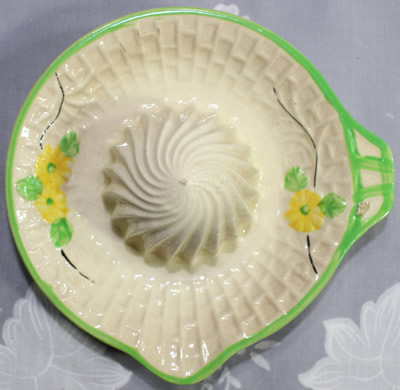 Top view of a yellow flowers on beige with green trim ceramic saucer juicer